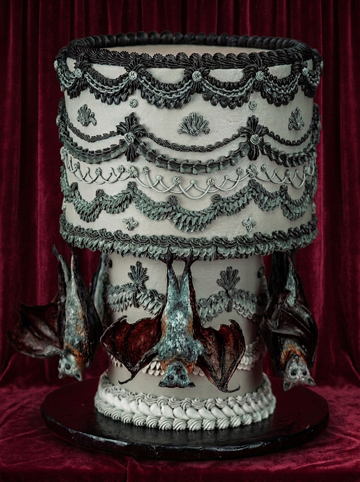 Pastel Lambeth vintage de dos pisos con overpiping en tonos hueso, gris y carbón y murciélagos decorativos colgando del piso superior, sobre terciopelo rojo