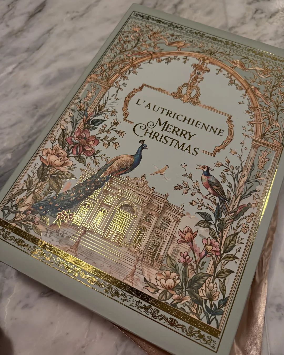 Calendario de Adviento L’Autrichienne 2026: portada con palacio, pavo real y foil dorado