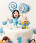 Detalle de figuritas de fondant de bebé y niña con paletas en espiral y globos azules sobre pastel de bautizo, L'Autrichienne CDMX